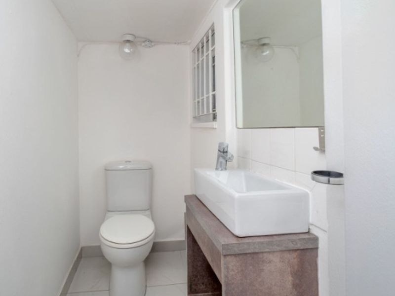 A compact, clean bathroom featuring a modern vessel basin on a vanity, a toilet, and a wall-mounted mirror.