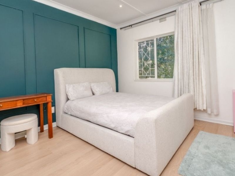 A well-maintained bedroom featuring laminate flooring, a decorative teal wainscoted accent wall, and recessed ceiling lighting.