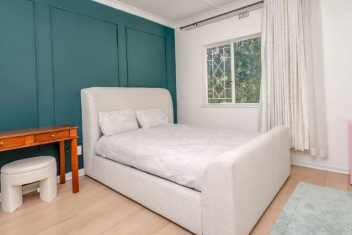 A well-maintained bedroom featuring laminate flooring, a decorative teal wainscoted accent wall, and recessed ceiling lighting.