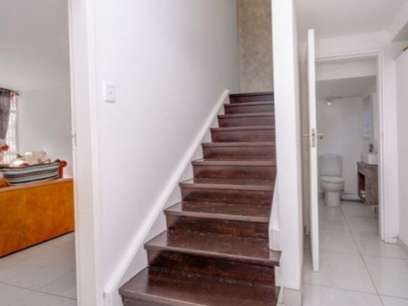 A bright hallway featuring a timber staircase with tiled flooring, providing access to adjacent living areas and a bathroom.