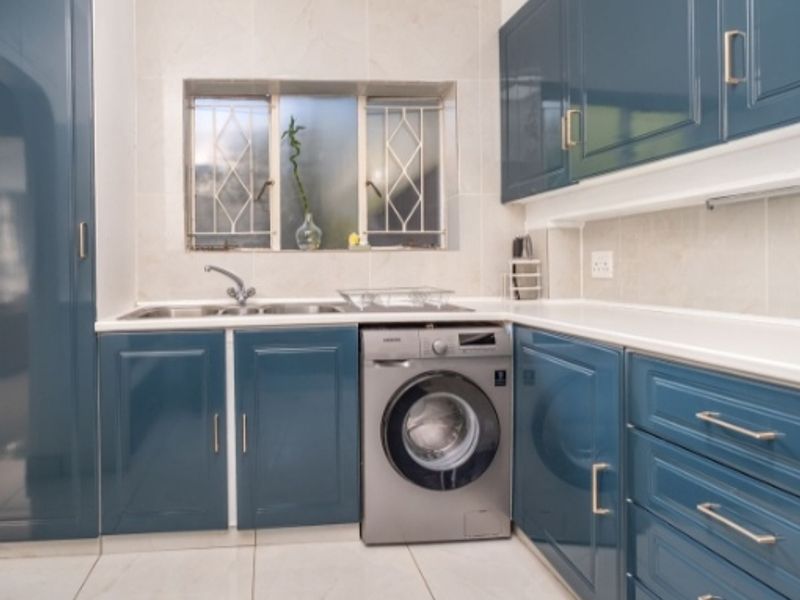A modern kitchen featuring high-gloss blue cabinetry, tiled flooring, a double sink, and a built-in washing machine with a tiled backsplash.