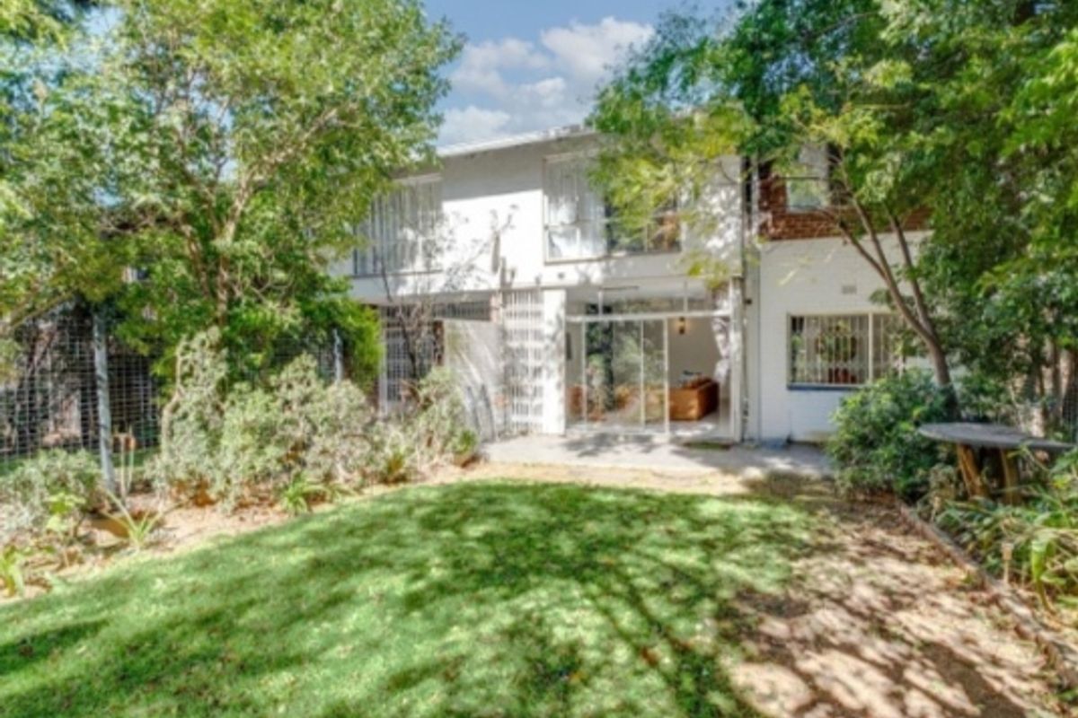 Rear view of the apartment building featuring a private garden, concrete patio area, and sliding glass doors with security bars.