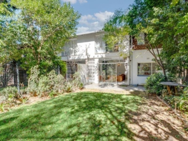 Rear view of the apartment building featuring a private garden, concrete patio area, and sliding glass doors with security bars.
