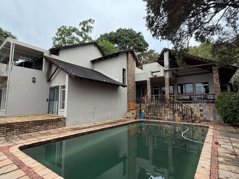 Rear exterior view featuring a swimming pool, covered patio area, and multi-level brick architecture set within a mature garden.