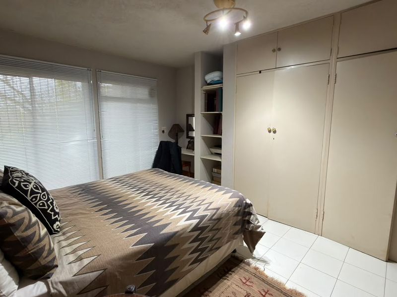 A bedroom featuring built-in cupboards, tiled flooring, and built-in shelving, offering functional storage space with natural light from large windows.
