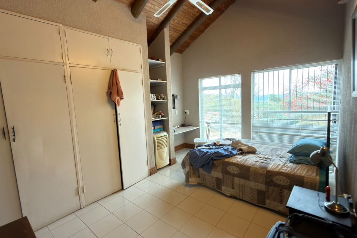 A bedroom featuring high exposed timber beam ceilings, tiled flooring, and extensive built-in cupboard storage with natural light from large windows.
