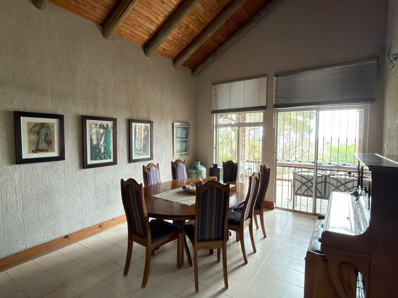 Spacious dining room featuring a high vaulted timber ceiling with exposed beams, tiled flooring, and sliding glass doors leading to an outdoor area.
