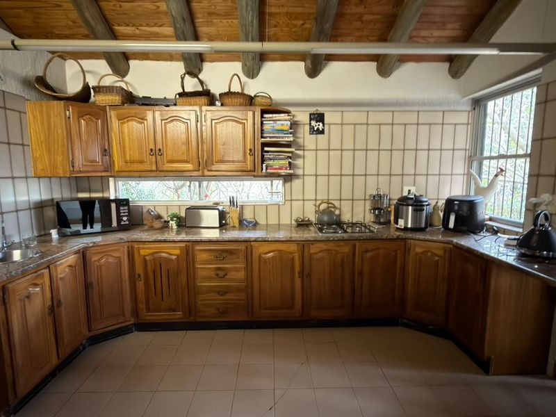 A traditional kitchen featuring wooden cabinetry, stone countertops, tiled backsplash, and exposed timber ceiling beams, offering a rustic aesthetic with functional workspace.