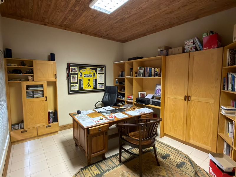 A functional home office featuring built-in wooden cabinetry, a warm timber ceiling, and tiled flooring, providing ample storage and workspace.