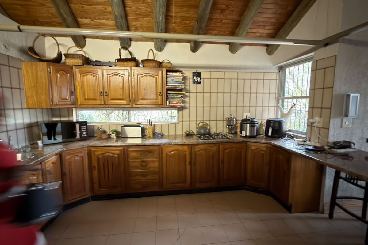 A rustic kitchen featuring wooden cabinetry, exposed timber ceiling beams, tiled backsplash, and a built-in breakfast counter, offering a traditional and functional cooking space.