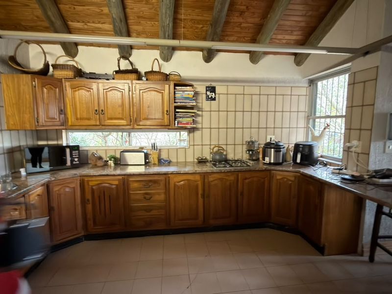 A rustic kitchen featuring wooden cabinetry, exposed timber ceiling beams, tiled backsplash, and a built-in breakfast counter, offering a traditional and functional cooking space.