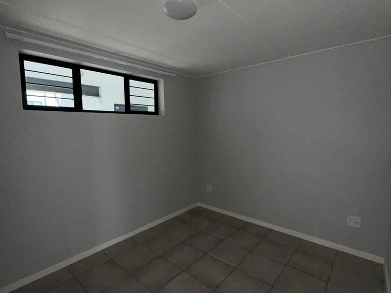 An empty bedroom featuring neutral grey walls, tiled flooring, and a high-level window with security bars.