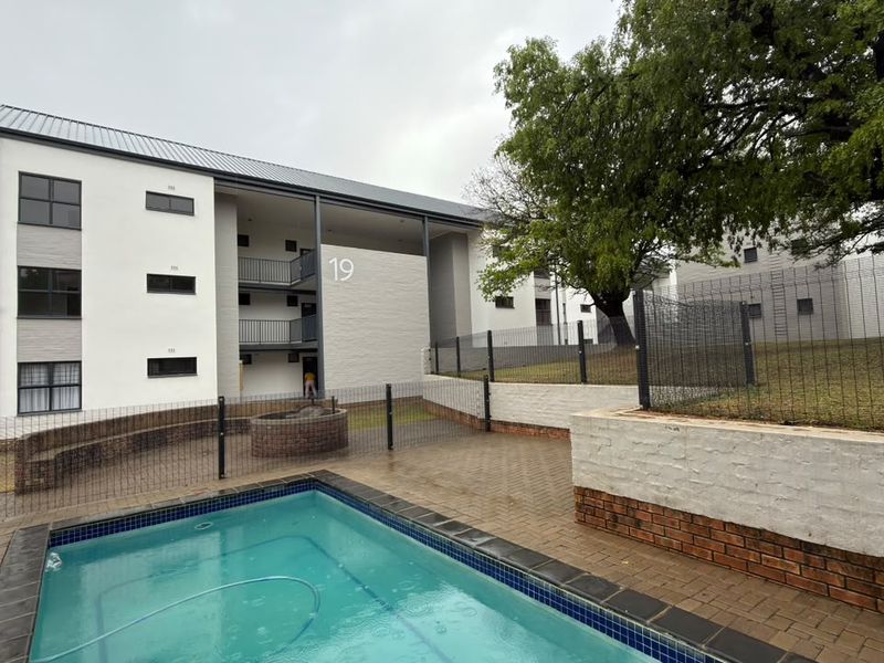 Outdoor pool area featuring a paved patio, brick retaining walls, and metal security fencing set against a multi-story apartment building.