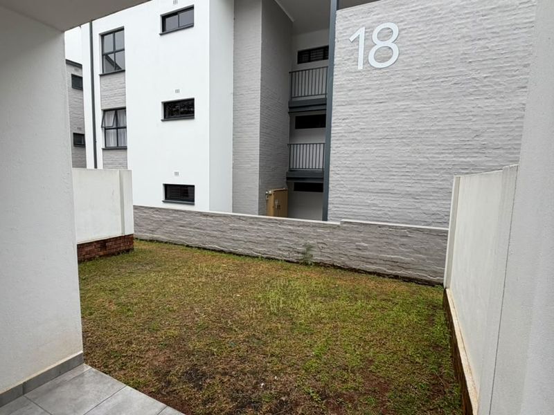 A private ground-floor garden area featuring a small lawn, boundary walls, and a tiled patio section adjacent to the apartment building.