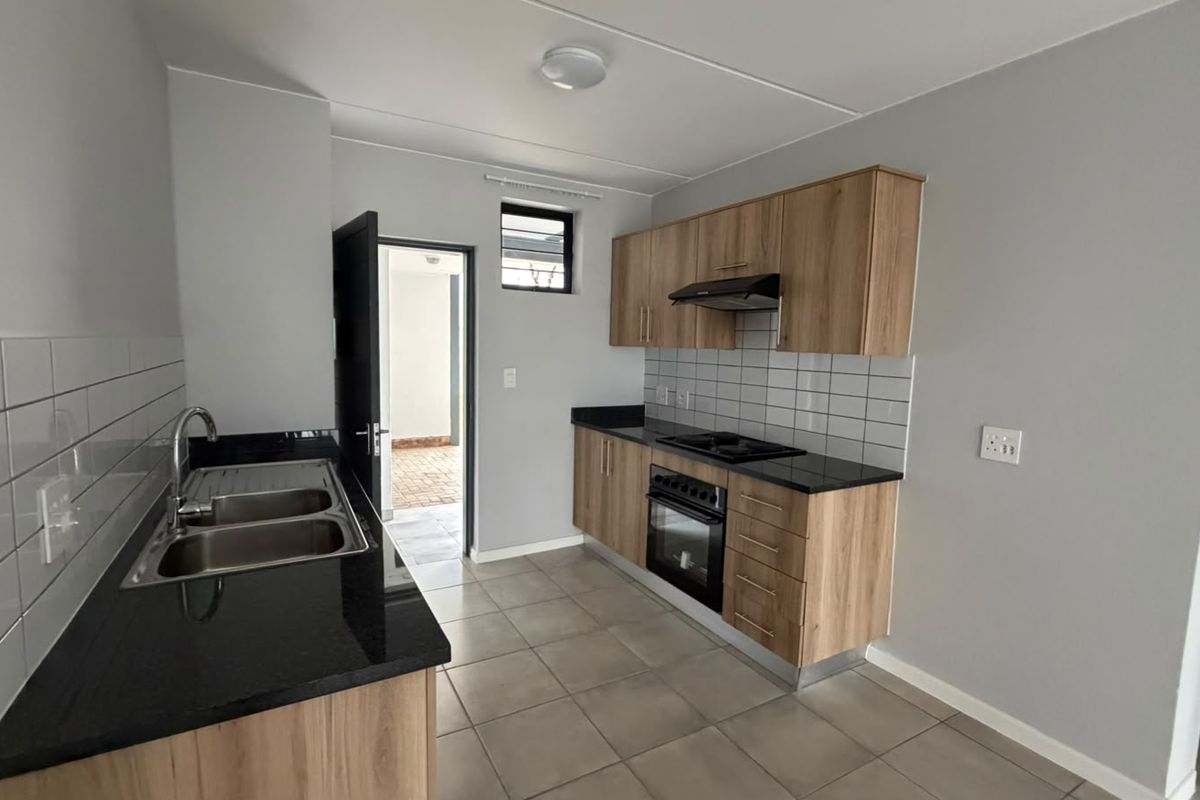 A clean, modern kitchen featuring light wood cabinetry, black granite countertops, a built-in oven, hob, extractor fan, and neutral tiled flooring.