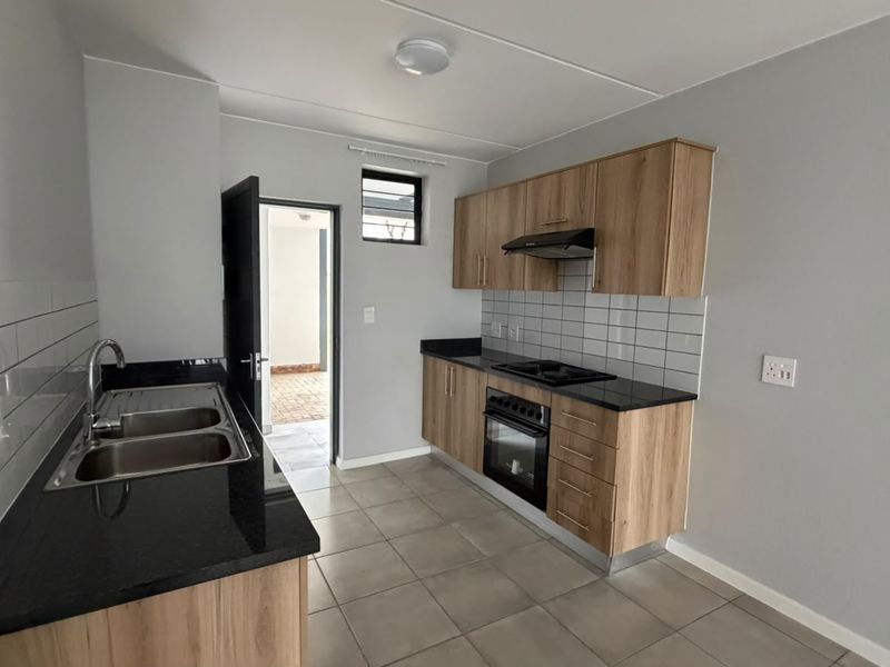 A clean, modern kitchen featuring light wood cabinetry, black granite countertops, a built-in oven, hob, extractor fan, and neutral tiled flooring.