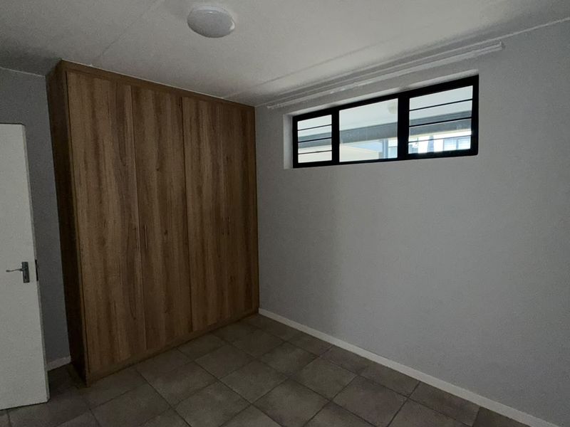 A clean, empty bedroom featuring neutral tiled flooring, built-in wooden cupboards, and a horizontal window providing natural light.
