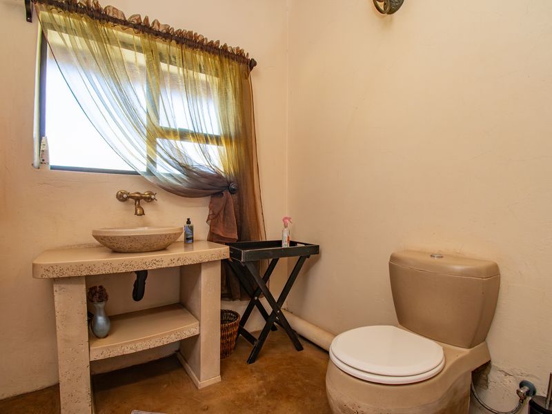 A rustic-style bathroom featuring a custom concrete vanity with a vessel sink, wall-mounted faucet, and a standard toilet.