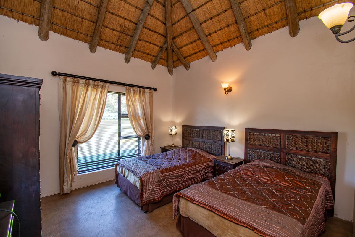 A rustic bedroom featuring a high vaulted thatched ceiling with exposed timber rafters and polished concrete flooring.