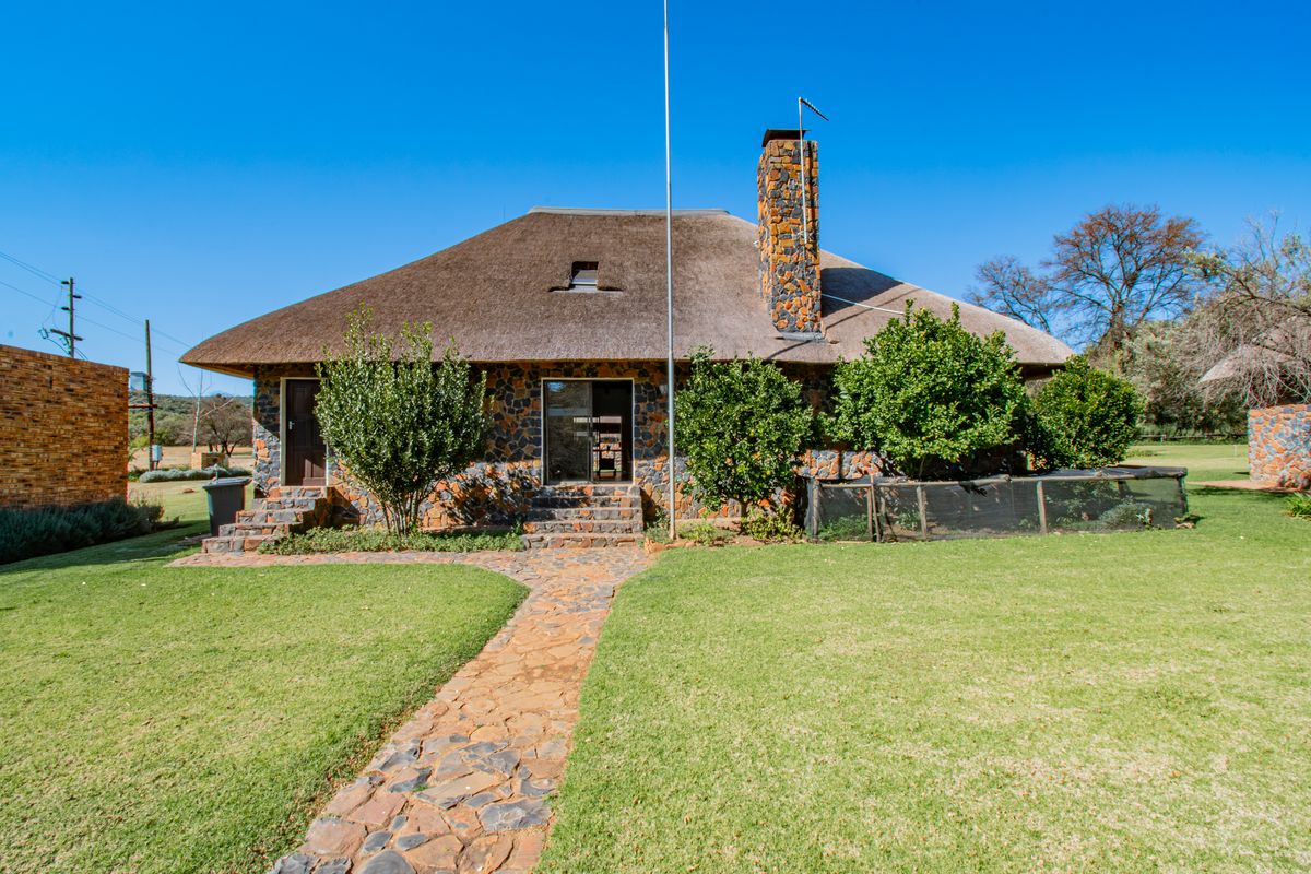 Rear view of a traditional farmhouse featuring stone cladding, a thatched roof, a prominent stone chimney, and a stone pathway leading to the entrance.