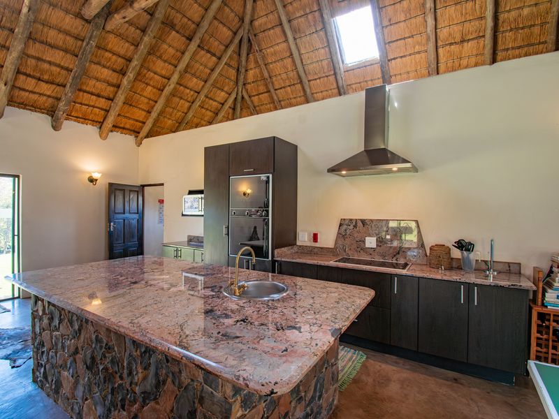 Spacious kitchen featuring a stone-clad island with granite countertops, built-in appliances, and a high vaulted thatched ceiling with a skylight.