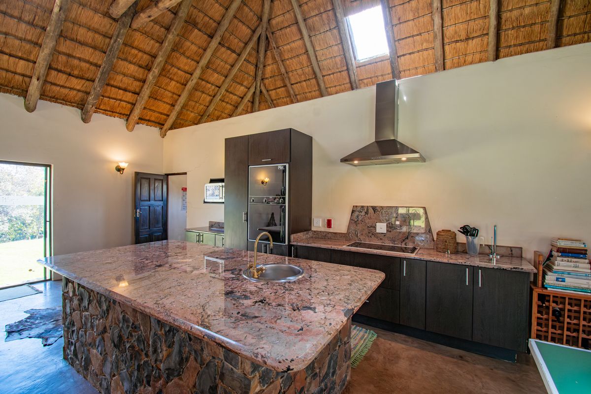 Spacious kitchen featuring a stone-clad island with granite countertops, built-in appliances, and a high vaulted thatched ceiling with a skylight.