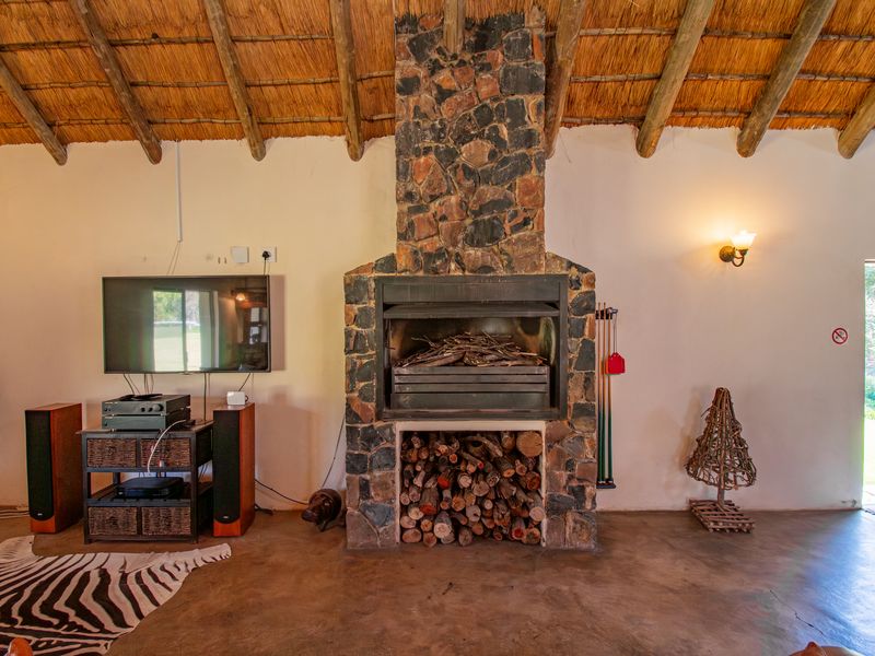 Spacious living area featuring a prominent stone fireplace, exposed timber rafters, and traditional thatched roofing, creating a rustic farm-style atmosphere.