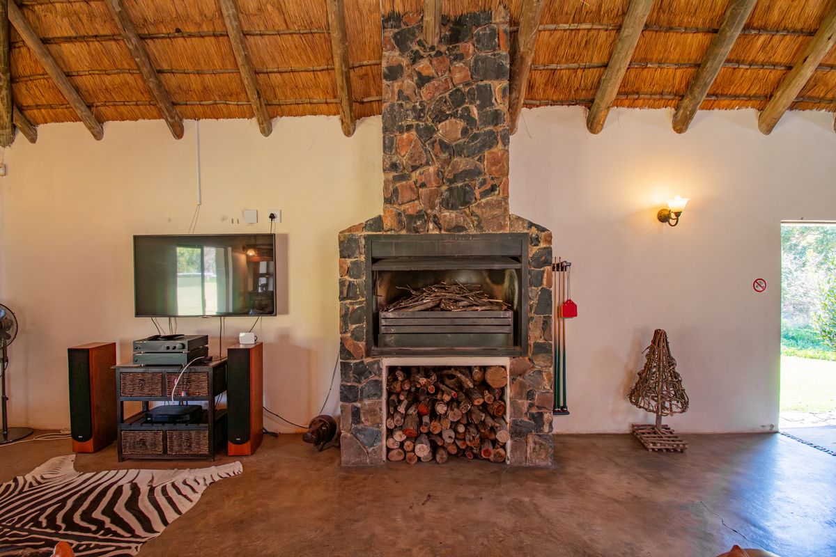 Spacious living area featuring a prominent stone fireplace, exposed timber rafters, and traditional thatched roofing, creating a rustic farm-style atmosphere.