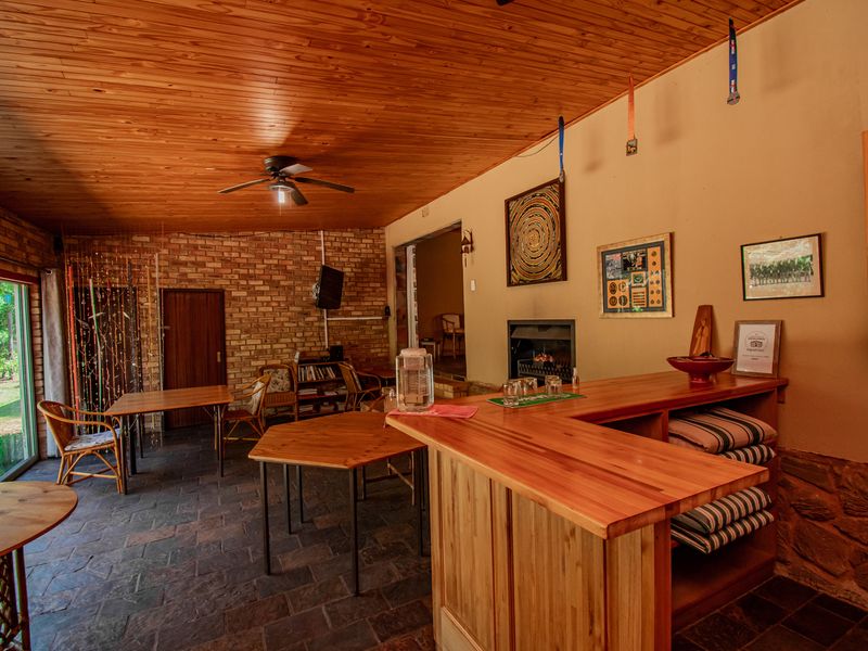 A rustic entertainment area featuring a built-in wooden bar, exposed brick walls, timber ceiling, and a cozy fireplace with direct access to the garden.