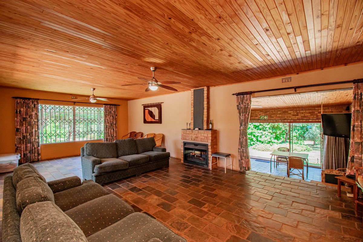Spacious living room featuring a timber ceiling, stone tile flooring, and a built-in brick fireplace, with direct access to an outdoor patio area.
