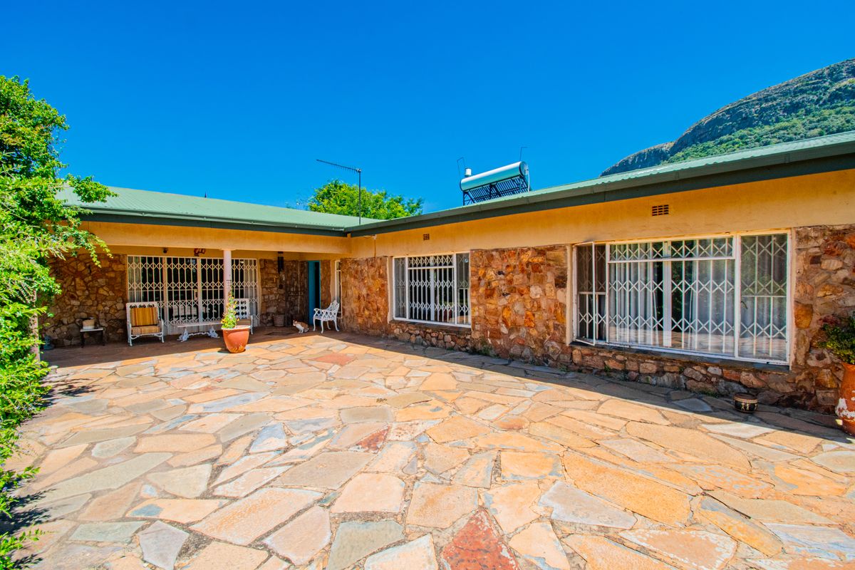 Spacious rear patio area featuring natural stone cladding, flagstone paving, and secure metal window bars, set against a scenic mountain backdrop.