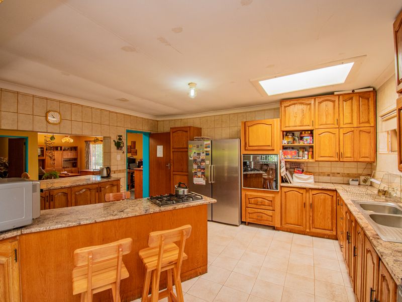 Spacious kitchen featuring wooden cabinetry, granite countertops, a built-in oven, gas hob, and a skylight, offering a functional layout with ample storage space.