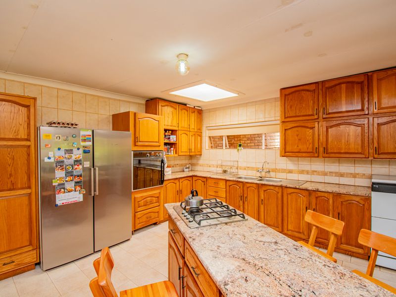 A functional kitchen featuring extensive wooden cabinetry, granite countertops, a central island with a gas hob, and a skylight for natural illumination.