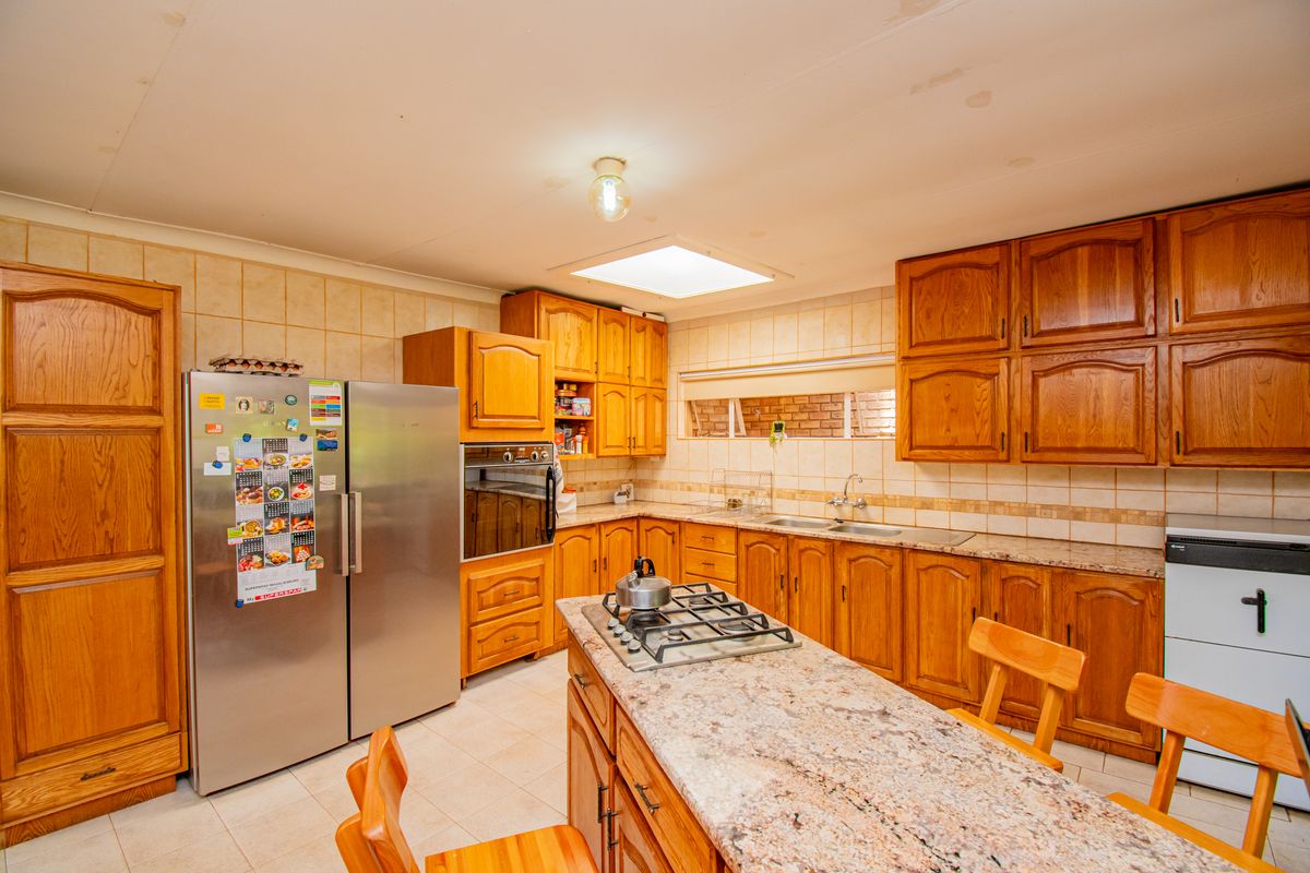 A functional kitchen featuring extensive wooden cabinetry, granite countertops, a central island with a gas hob, and a skylight for natural illumination.