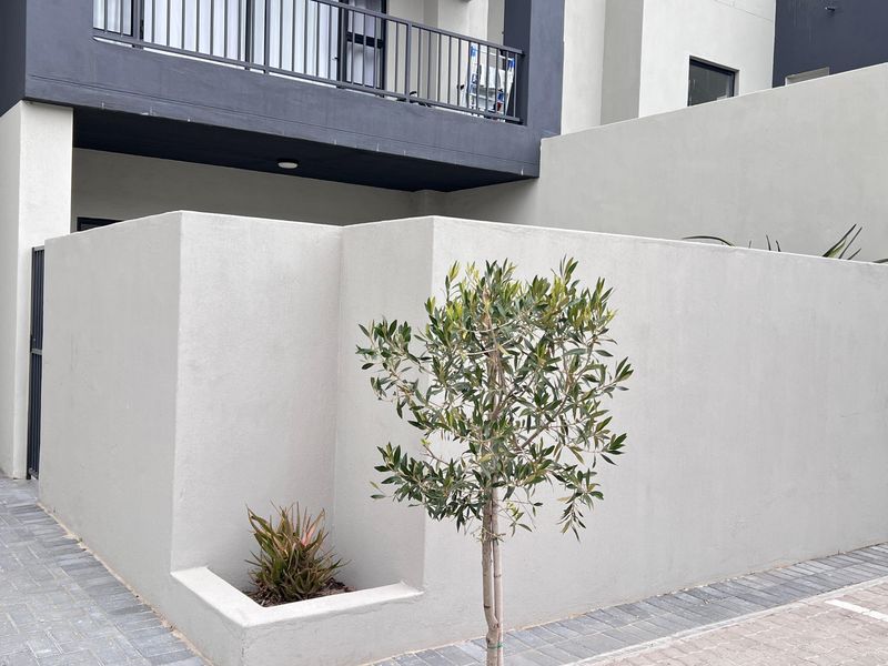 Modern apartment exterior featuring a paved driveway, clean rendered boundary walls, and a balcony with metal railings.