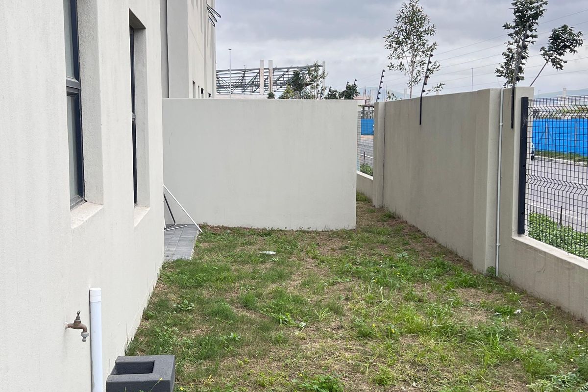 A rear exterior view of the apartment featuring a private garden area with boundary walls, paving, and an external water tap.