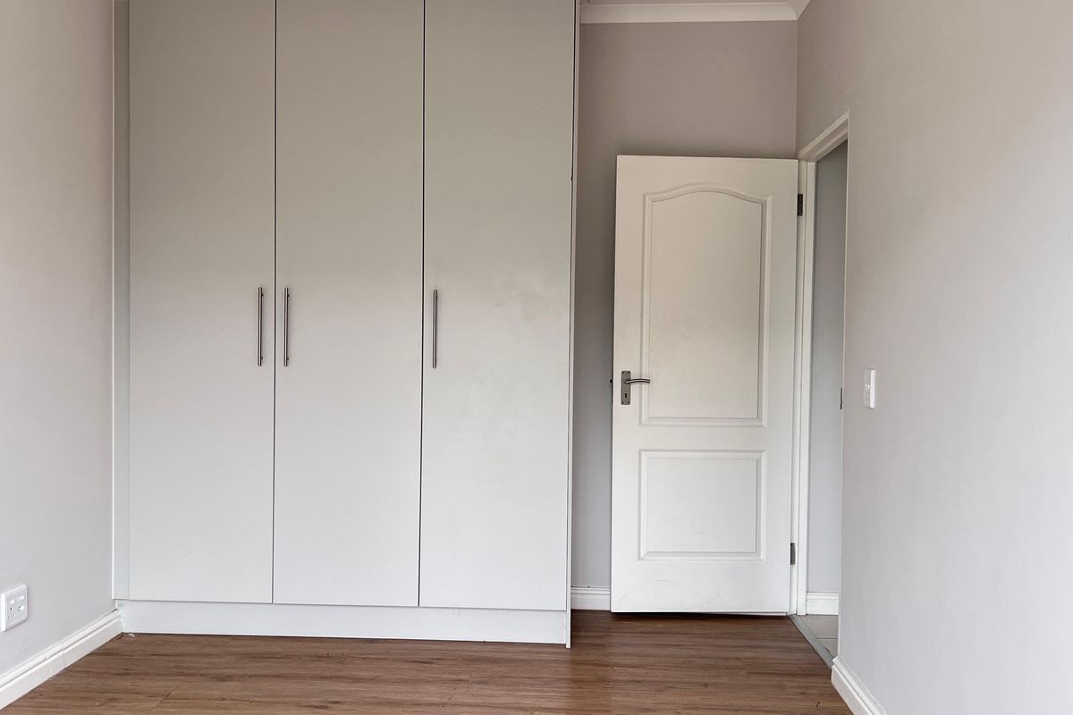 A clean, empty bedroom featuring neutral walls, laminate flooring, and a large built-in wardrobe with modern handles.