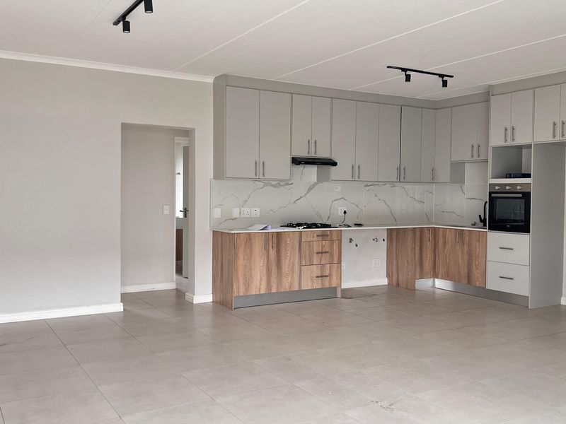 Modern open-plan kitchen featuring two-tone cabinetry, marble-look splashback, built-in oven, gas hob, and neutral tiled flooring in a spacious, well-lit living area.