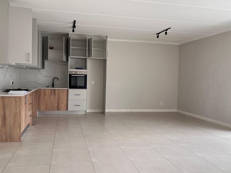 Modern open-plan kitchen and living area featuring sleek cabinetry, built-in oven, gas hob, marble-look splashback, and neutral tiled flooring throughout.