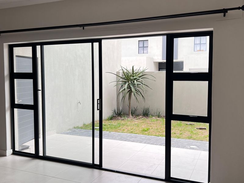 Bright living area featuring large black aluminium sliding doors that open onto a private paved patio and small garden space.