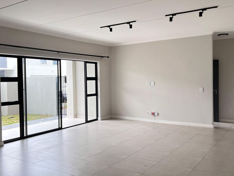 Spacious, modern open-plan living area featuring neutral tiled flooring, track lighting, and large sliding glass doors providing access to the outdoor space.
