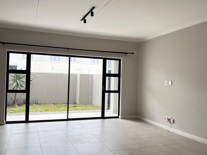 A bright, open-plan living area featuring neutral tiled flooring, modern track lighting, and large sliding glass doors providing access to the outdoor space.
