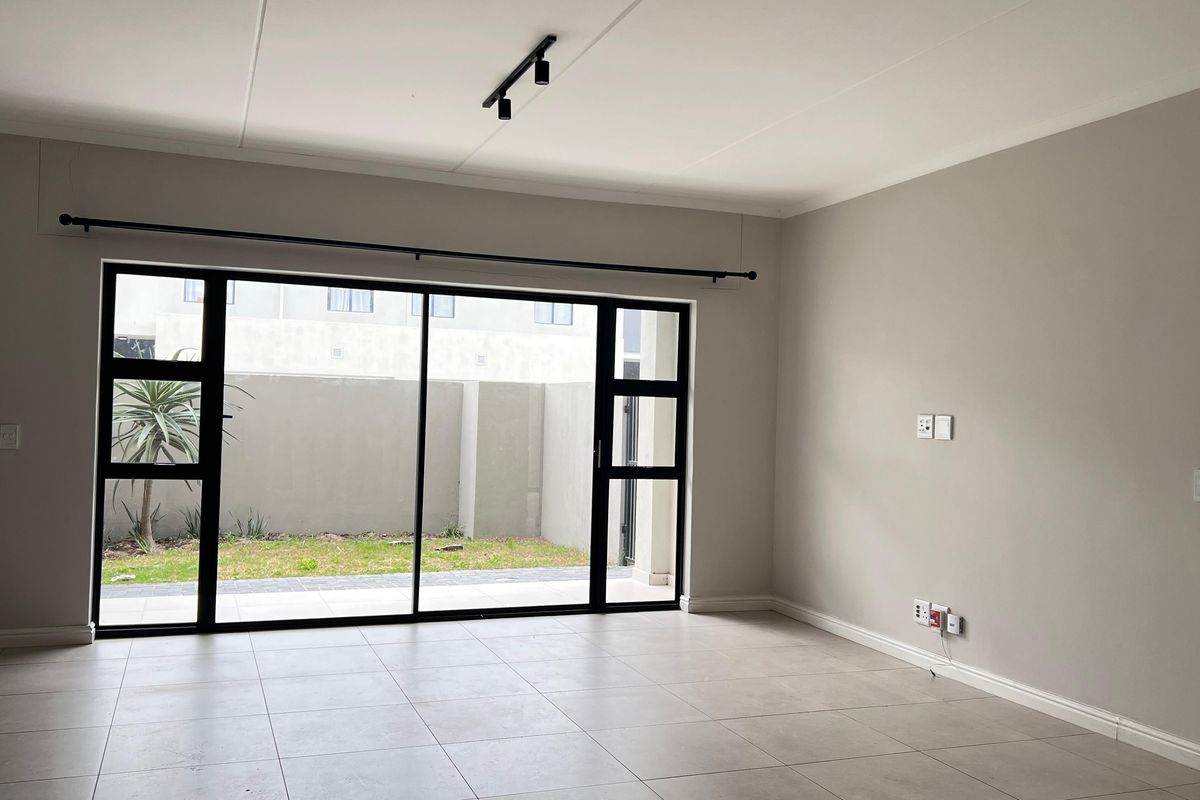 A bright, open-plan living area featuring neutral tiled flooring, modern track lighting, and large sliding glass doors providing access to the outdoor space.