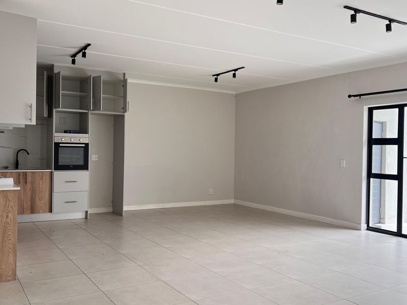 Spacious open-plan living area featuring modern kitchen cabinetry, built-in oven, gas hob, tiled flooring, and direct access to an outdoor area via sliding doors.