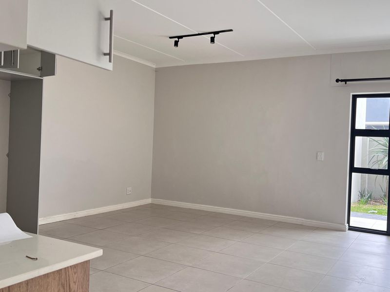 An open-plan living and kitchen area featuring neutral tiled flooring, modern track lighting, and a sliding glass door leading to the exterior.