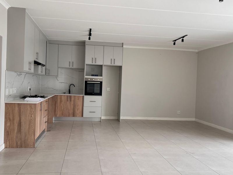 Modern open-plan kitchen and living area featuring contemporary cabinetry, built-in oven, gas hob, and neutral tiled flooring in a clean, vacant space.