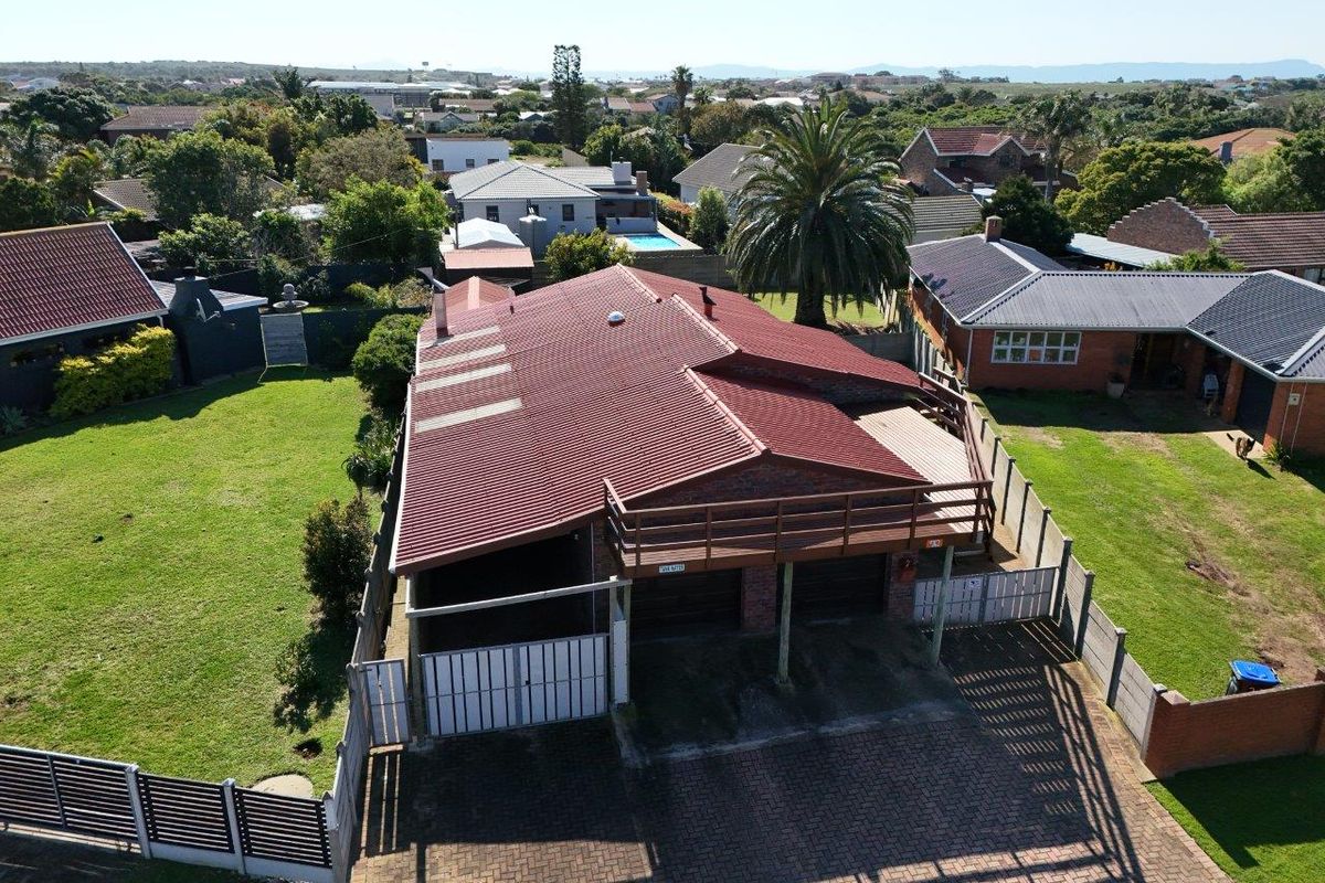 Aerial view of a residential property featuring a corrugated metal roof, brick exterior, double garage, and a raised wooden balcony overlooking the garden.