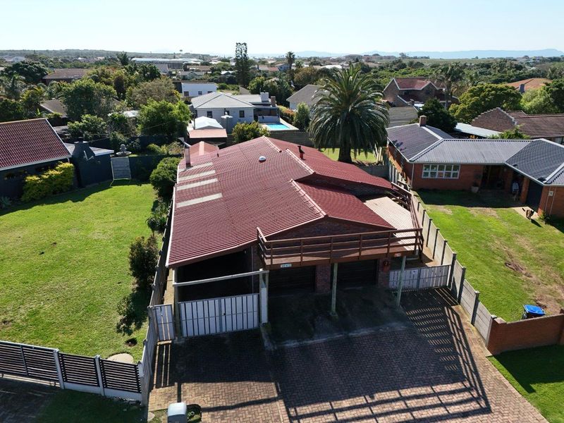 Aerial view of a residential property featuring a corrugated metal roof, brick exterior, double garage, and a raised wooden balcony overlooking the garden.