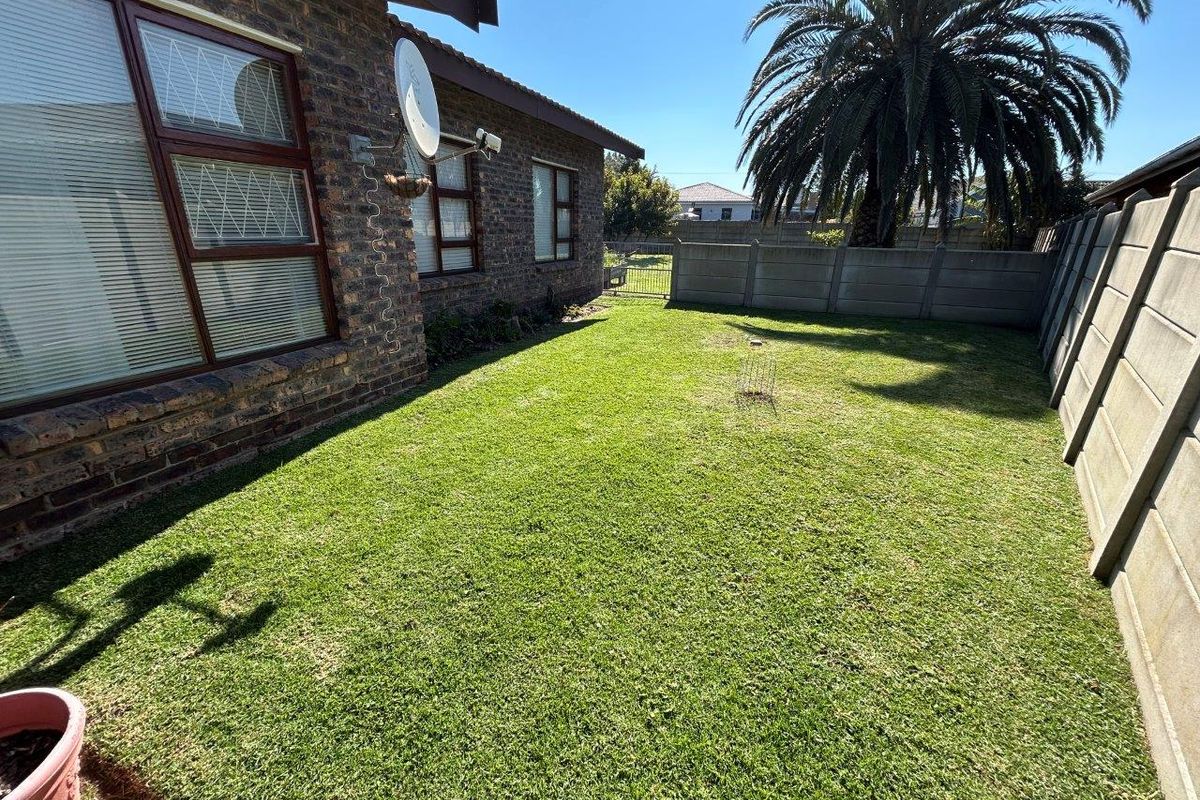 A private rear garden featuring a well-maintained lawn, enclosed by precast concrete boundary walls and adjacent to the face brick exterior of the house.