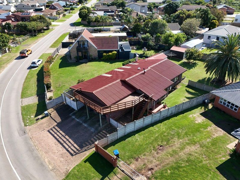 Aerial view of a residential property featuring a corrugated metal roof, a raised wooden deck, and a paved driveway within a fenced garden.